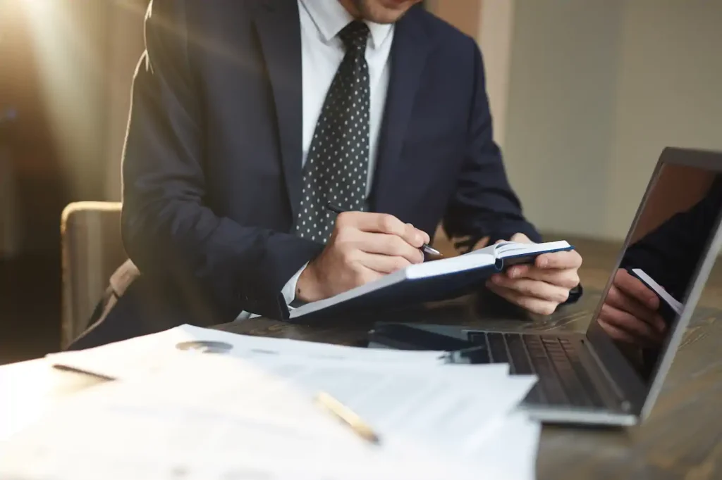 Hombre de negocios escribiendo en libreta junto a laptop