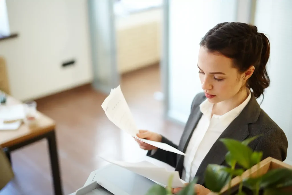 Mujer revisando documentos junto a impresora en oficina