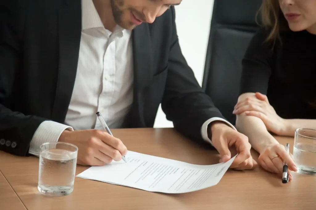 Hombre firma contrato junto a mujer en oficina