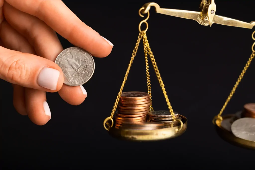 Mano sostiene moneda junto a balanza con monedas